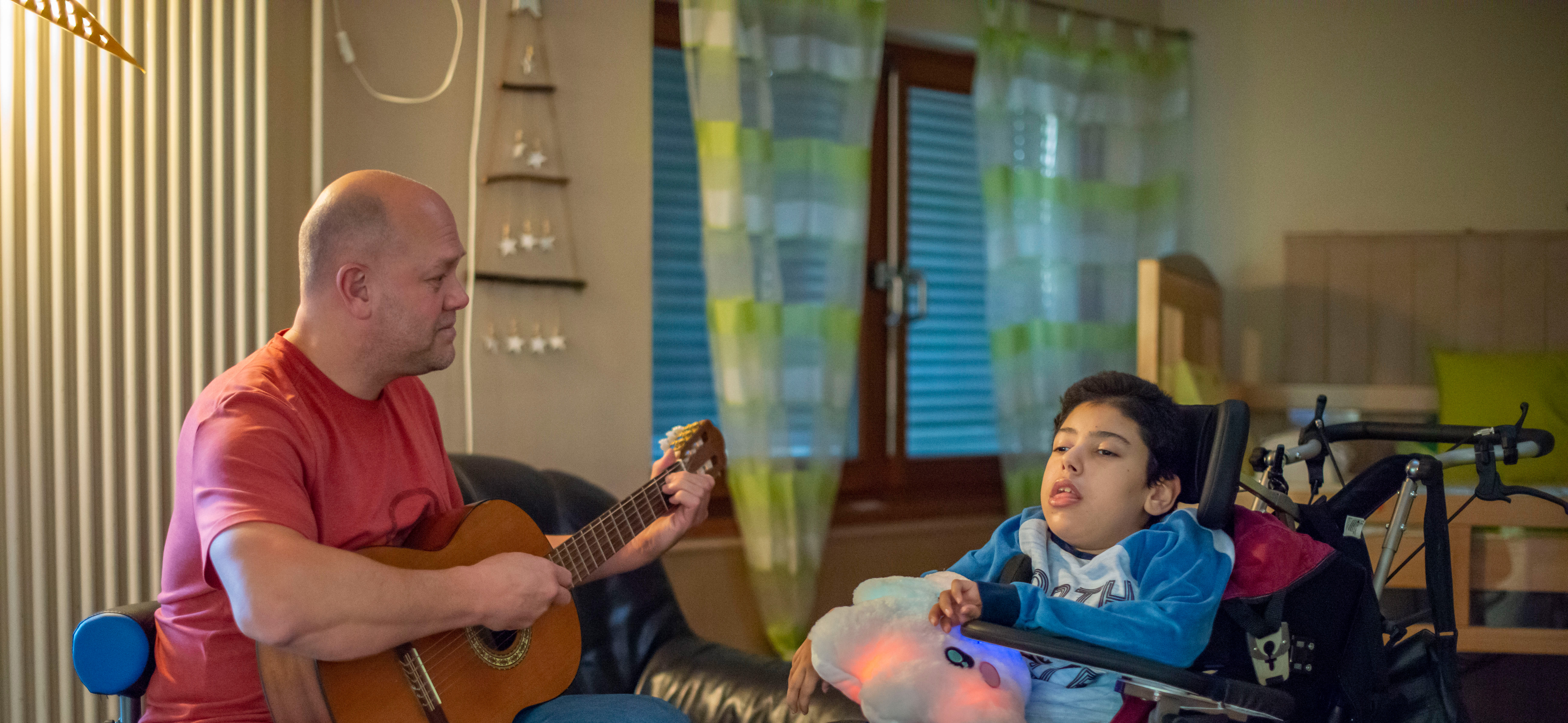 Ein Mitarbeitender aus dem Bereich Wohnen musiziert gemeinsam mit einem Jungen im Rollstuhl.