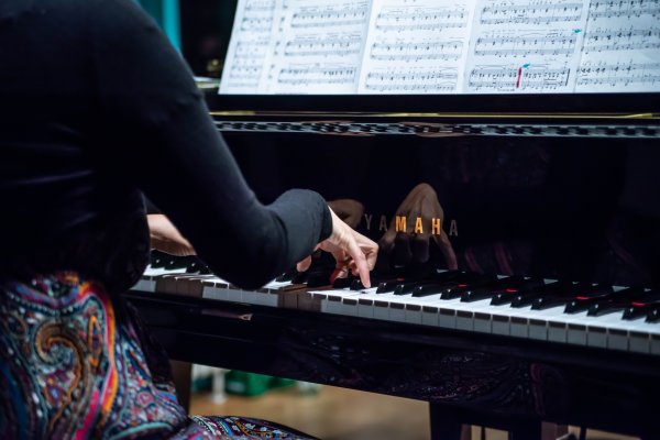 Eine Klavierspielerin spielt auf einem Flügel. Der Bildausschnitt liegt auf ihren Händen, den Tasten und den Noten.