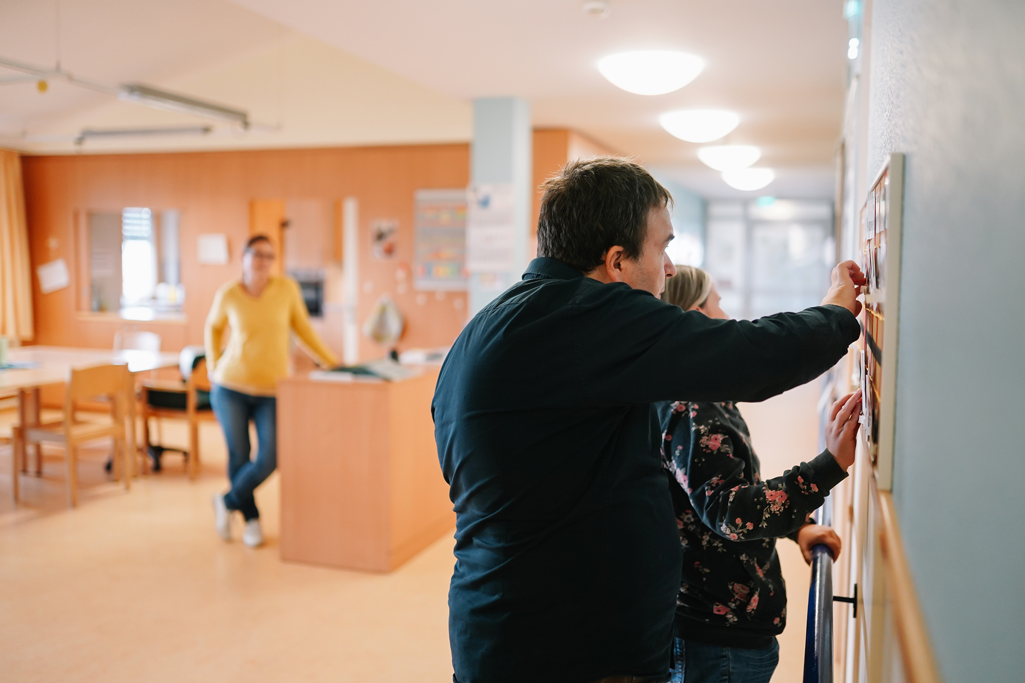 Ein blinder Mann und eine blinde Frau stehen an einer Infotafel und ertasten Informationen in Brailleschrift