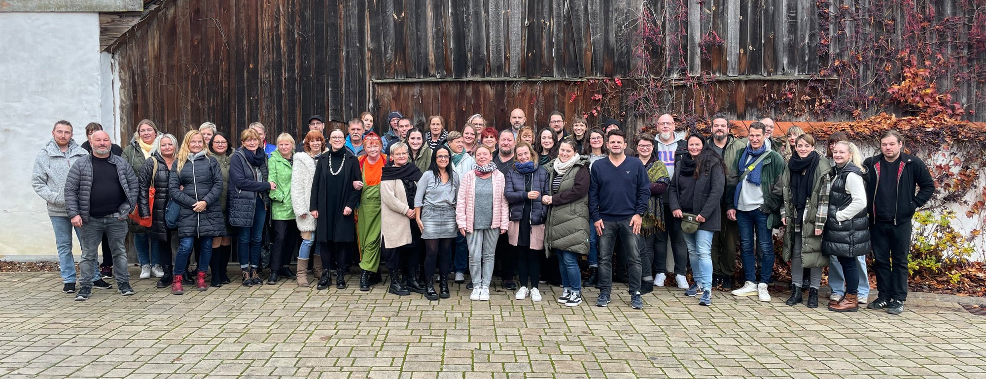 Gruppenfoto des Personalrats: Auf einem gepflasterten Platz vor einer Scheune steht eine große Gruppe von ungefähr 50 Menschen mit dicken Winterjacken. Die Menschen blicken in die Kamera und lächeln.
