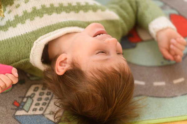 Ein Kind liegt auf einem Spielteppich und lächelt.